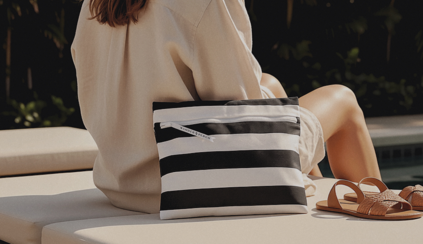 Person sitting by a pool with a black and white striped bag and brown sandals.