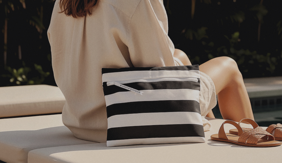 Person sitting by a pool with a black and white striped bag and brown sandals.
